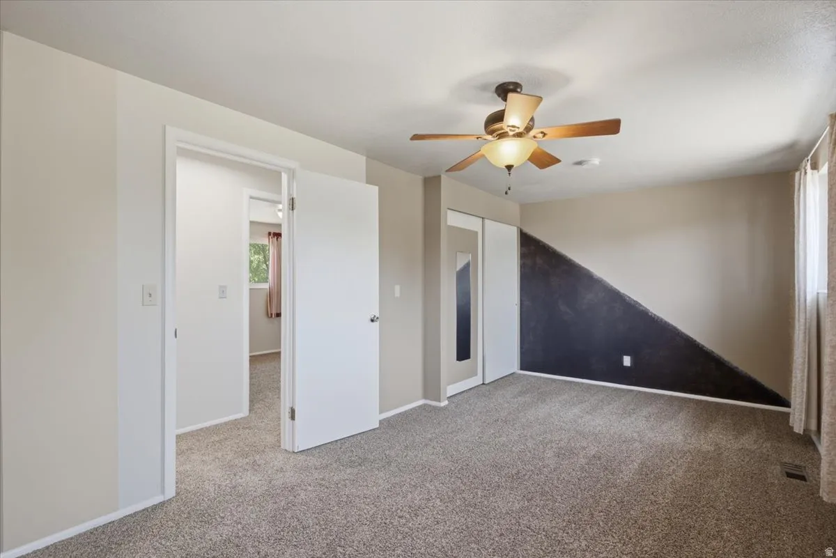 Carpeted room featuring a ceiling fan with integrated lighting, a contrasting accent wall, and dual sliding closet doors
