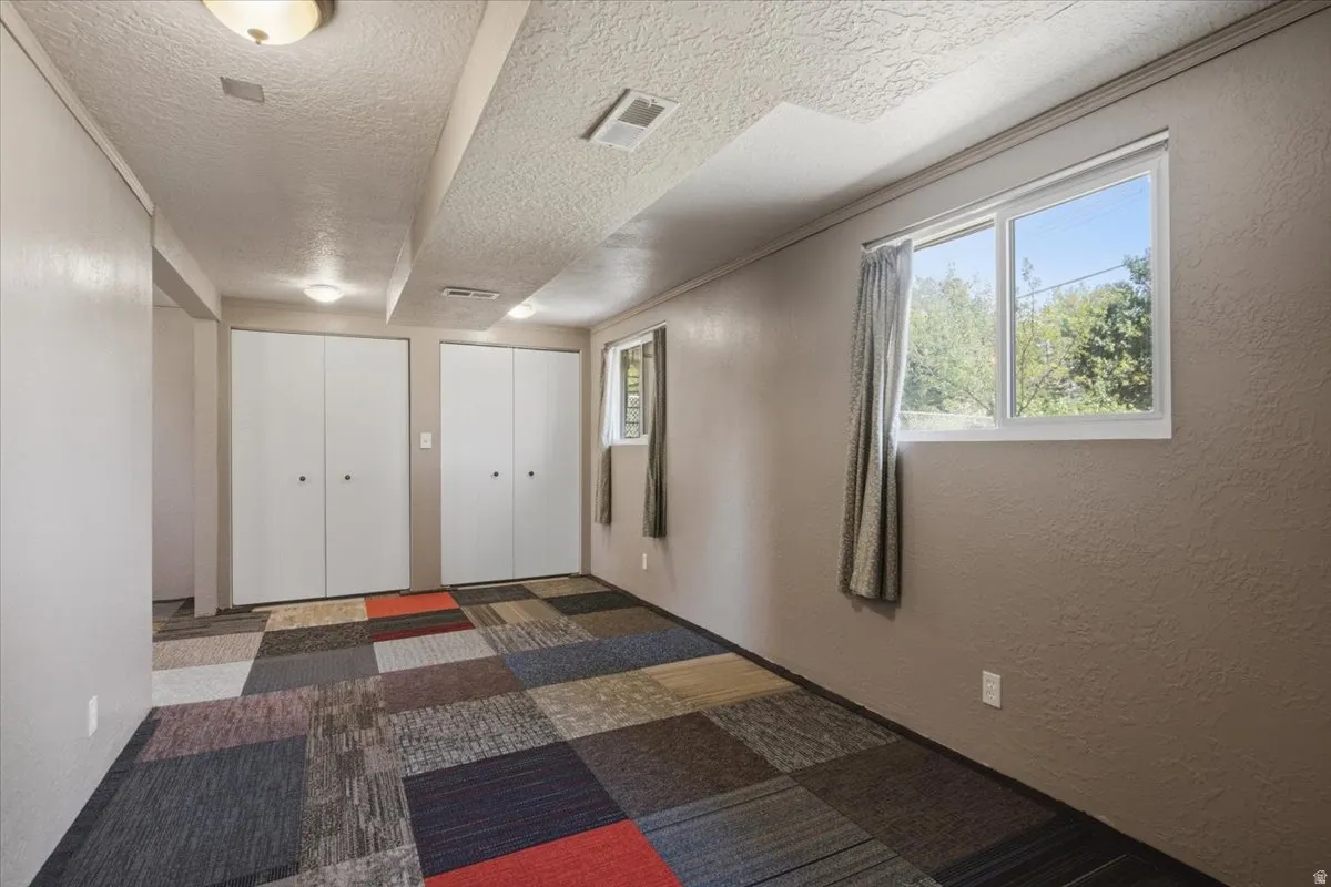 Room featuring multi-colored carpet tile flooring, two white bi-fold closet doors, and two windows with white trim