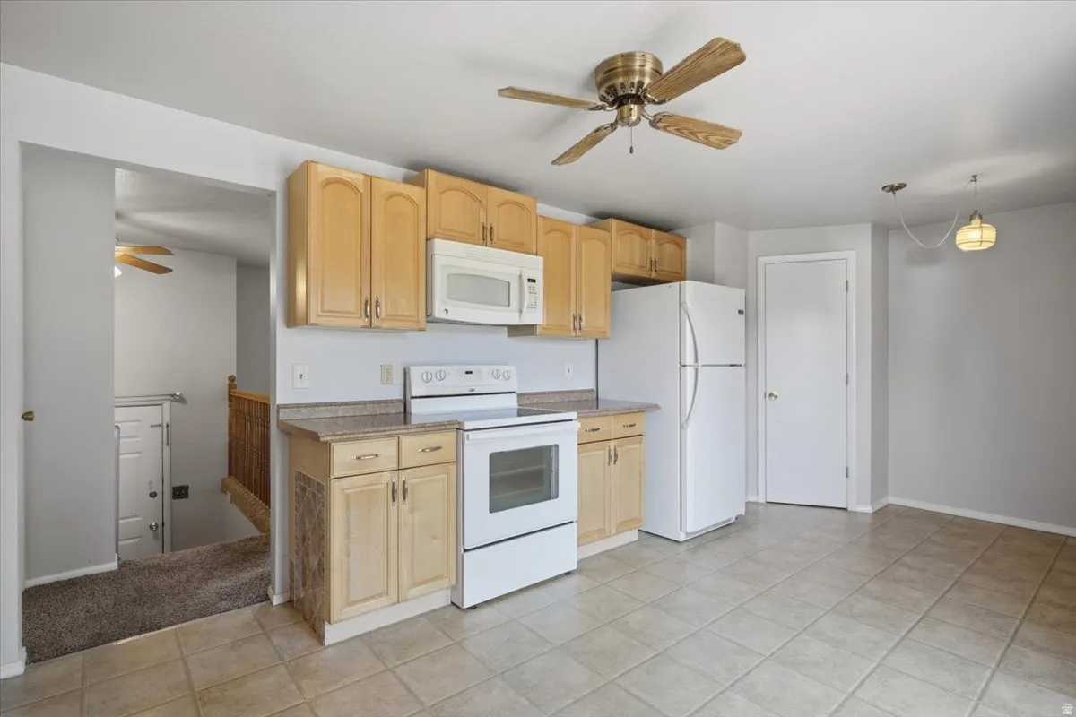Kitchen featuring light wood-finish cabinetry, white appliances, and tiled flooring