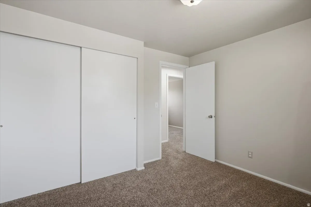 Bedroom featuring neutral carpeting, light gray wall paint, white trim, a ceiling-mounted light fixture, and a sliding closet door system