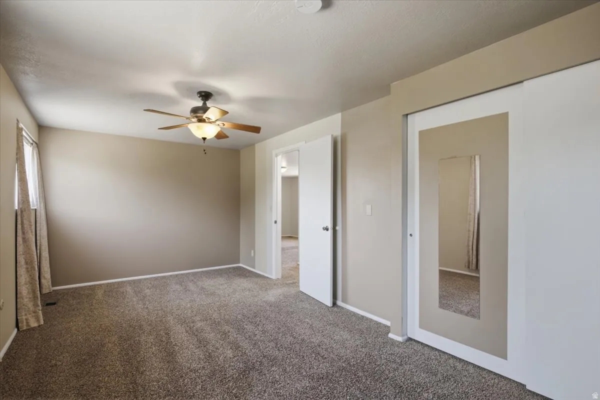 Carpeted interior room featuring a ceiling fan with integrated lighting, a mirrored sliding closet door, and a window with drapes