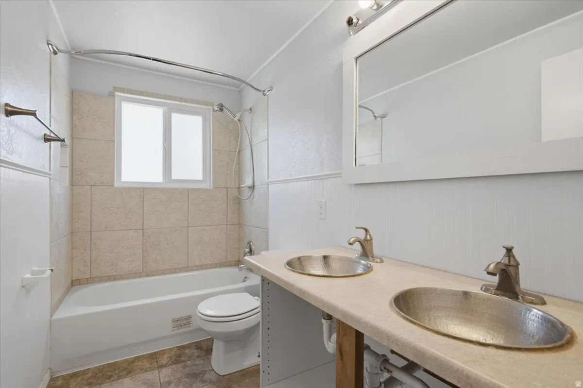 Bathroom featuring a double vanity with unique basin sinks, a framed mirror, and a tub-shower combination with tiled surround