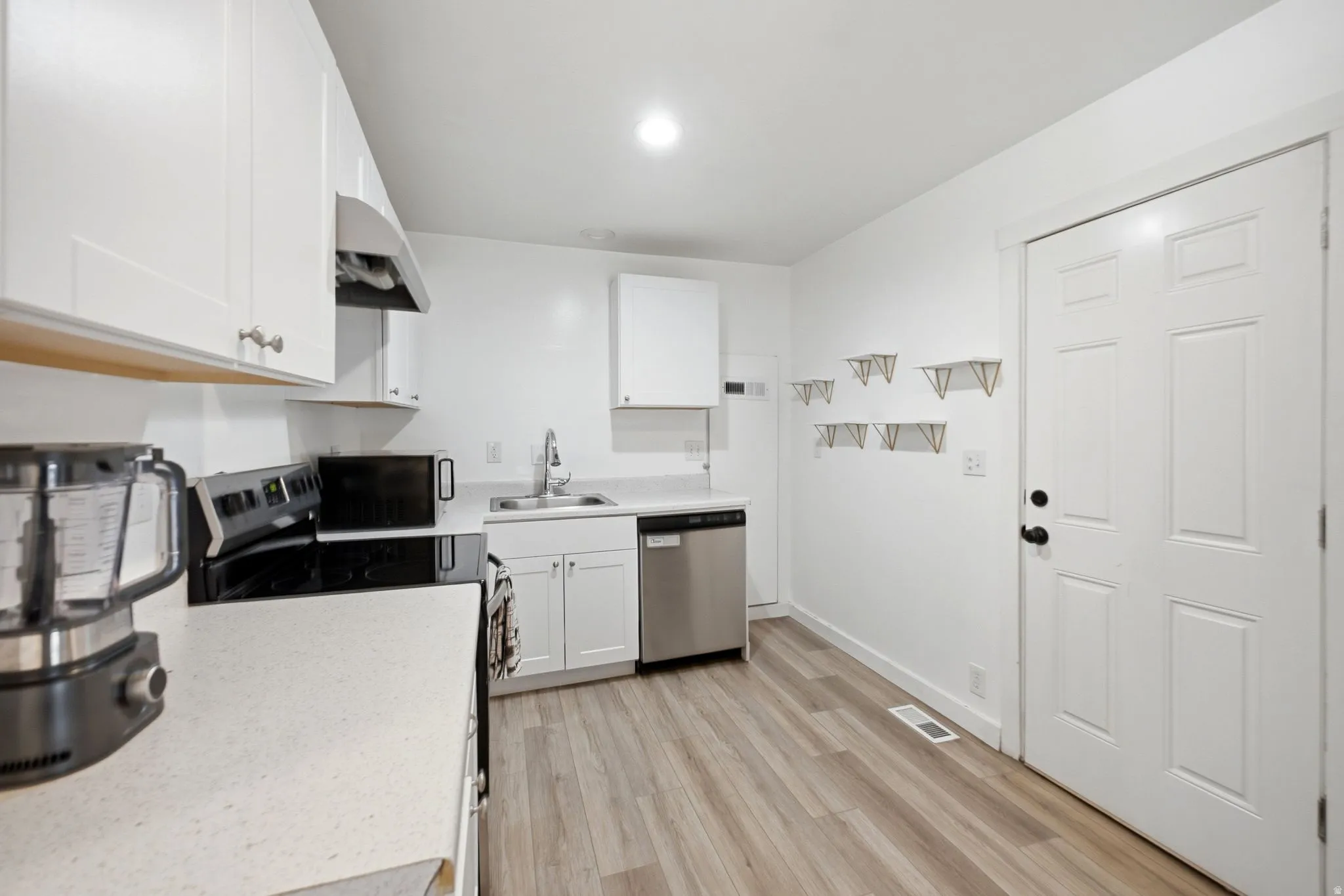Kitchen featuring white cabinetry, light-toned countertops, wood-finish flooring, a stainless steel dishwasher, and a range with an overhead exhaust hood