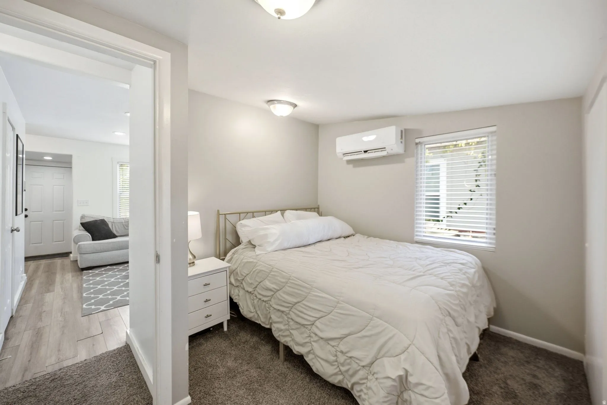 Bedroom featuring a ceiling-mounted light fixture, wall-mounted climate control unit, and window with horizontal blinds