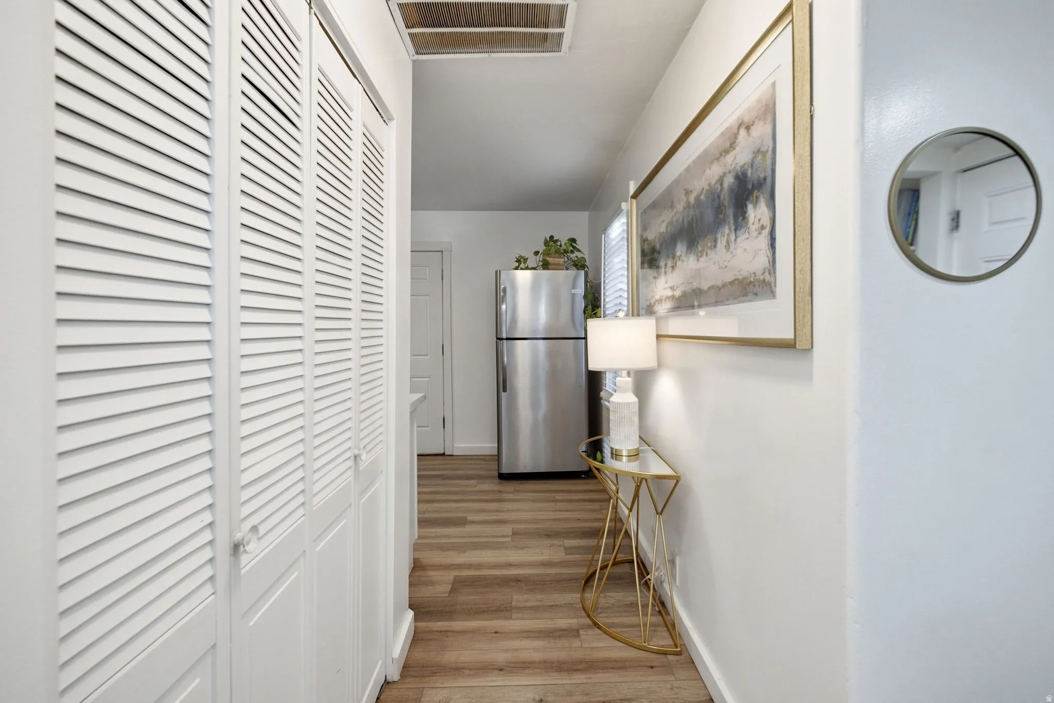 Hallway featuring wood-finish flooring, white louvered bifold doors, and a stainless steel refrigerator