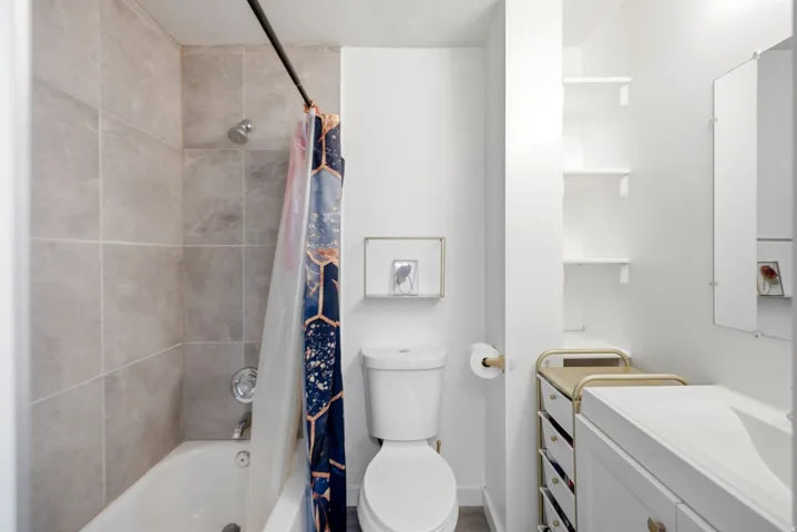 Full bathroom featuring a tub-shower combination with light gray tile surround, a white toilet, and a white vanity with an integrated sink