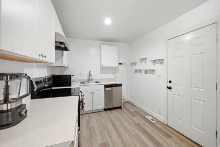Kitchen featuring white cabinetry, light-toned countertops, wood-finish flooring, a stainless steel dishwasher, and a range with an overhead exhaust hood