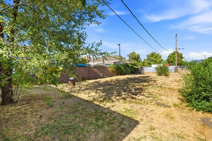 Expansive cleared lot featuring partial perimeter fencing, mature trees and shrubs, and a clear sky backdrop