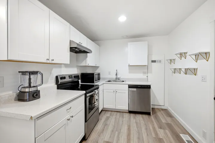 Contemporary kitchen featuring white cabinetry, light-toned countertops, stainless steel appliances, and wood-finish flooring