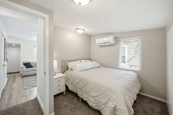 Bedroom featuring a ceiling-mounted light fixture, wall-mounted climate control unit, and window with horizontal blinds