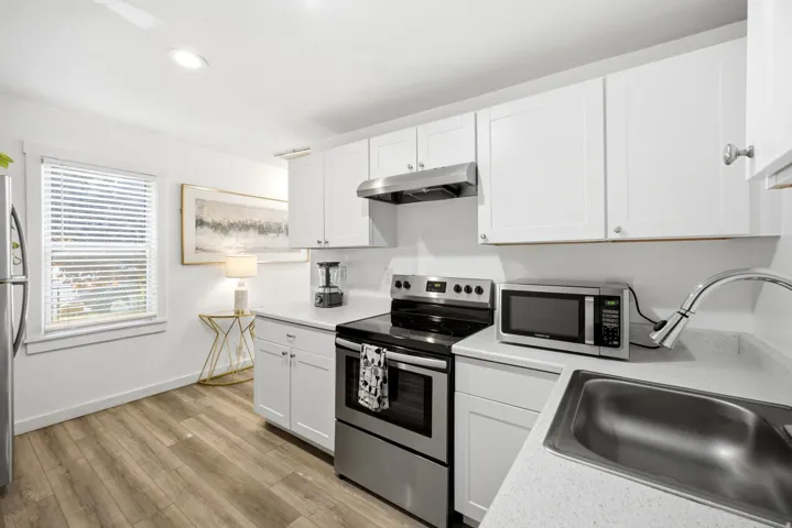 Kitchen featuring white shaker-style cabinetry, light-toned countertops, stainless steel appliances, a stainless steel sink with a gooseneck faucet, and wood-finish flooring
