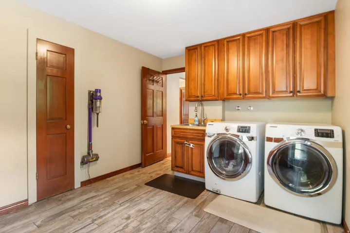Dedicated laundry room featuring wood-finish flooring, ample upper cabinetry, a utility sink with lower cabinetry, and two solid panel doors