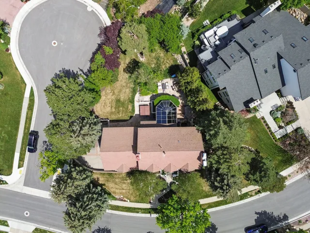 Aerial perspective showcasing a property with a distinct architectural feature, multiple mature trees, and a paved cul-de-sac