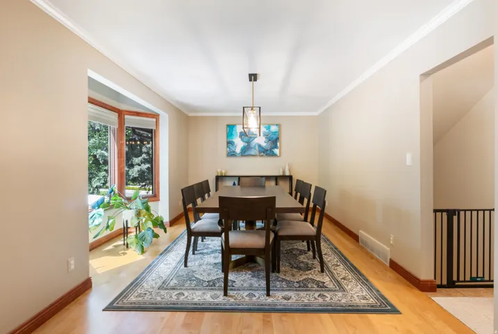 Spacious dining area featuring wood-finish flooring, a bay window with wood trim, crown molding, and a contemporary chandelier