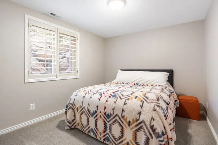 Bedroom featuring a daylight window with white plantation shutters, neutral paint, gray carpet flooring, white baseboards, and a flush-mount ceiling light fixture