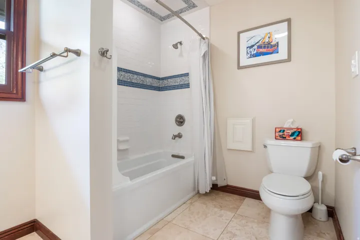 Bathroom featuring a white bathtub and shower combination with tiled surround, a mosaic accent band, and integrated shower fixtures