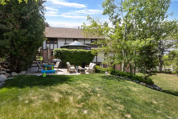 Expansive backyard featuring a manicured lawn, established trees, a stone retaining wall, and a multi-level patio with ample space for outdoor entertaining