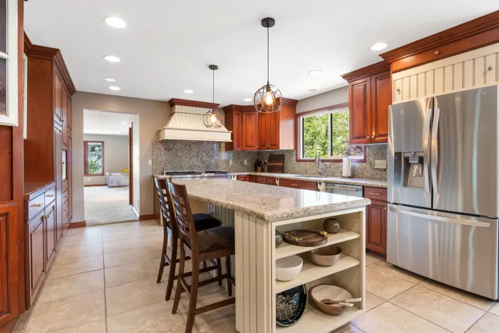 Open-concept kitchen featuring granite countertops, cherry wood cabinetry, stainless steel appliances, a center island with built-in shelving, and recessed lighting