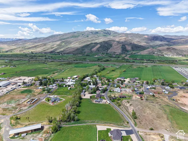 Expansive rural landscape featuring a mountainous backdrop, verdant fields, a residential area, and agricultural structures