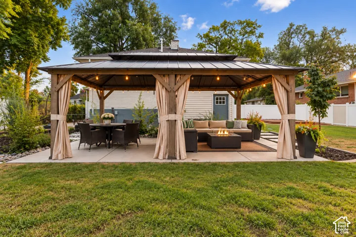Expansive concrete patio with gazebo structure featuring a tiered roof and privacy curtains. AI photo of evening.