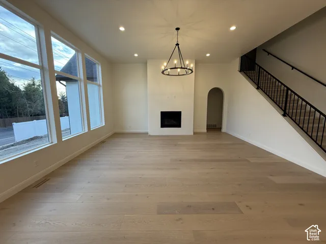Expansive living area featuring large windows, wood-finish flooring, a contemporary fireplace with a sleek surround, and a striking black chandelier