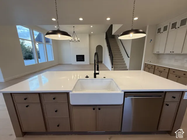 Expansive kitchen island featuring a farmhouse sink, stainless steel dishwasher, and light wood-finish cabinetry