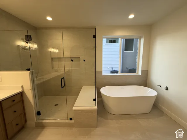 Freestanding soaking tub, walk-in shower with glass enclosure, integrated shower bench, recessed shower niche, and vanity with stone-finish countertop
