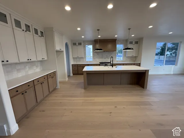 Spacious kitchen featuring an extended island with a built-in sink, white shaker-style upper cabinetry, wood-finish lower cabinetry, light wood-finish flooring, and recessed lighting