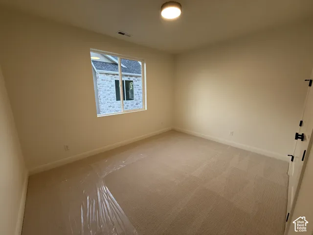 Neutral tone wall paint, light-toned carpet flooring, a single window, a flush-mount ceiling light fixture, and a door with dark hardware