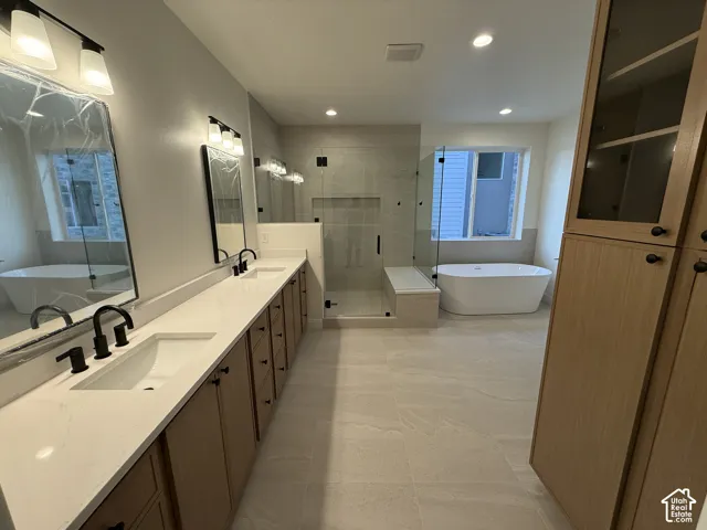 Dual vanities with quartz countertops, a freestanding soaking tub, a glass-enclosed shower, built-in cabinetry, and large format tile flooring