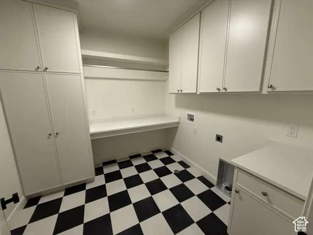 Checkerboard flooring, extensive white cabinetry, built-in countertop with hanging rod, additional counter space, and utility connections