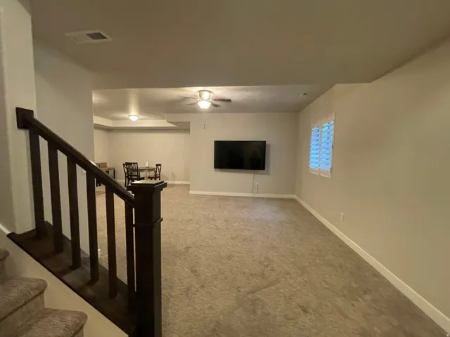 Carpeted lower level with a recessed ceiling, ceiling fan, and window featuring plantation shutters