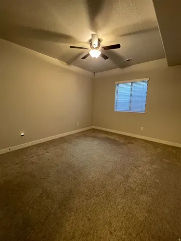 Wall-to-wall carpeting with a neutral color palette, a single window with blinds, and a ceiling fan with integrated lighting