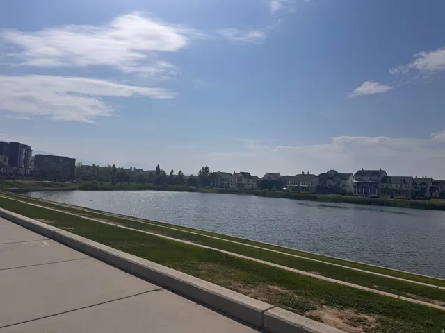 Waterfront property featuring a concrete walking path, sloped grassy areas, and a residential neighborhood across the water