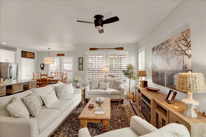 Open-concept living space featuring wood-finish flooring, a ceiling fan, and large windows with plantation shutters