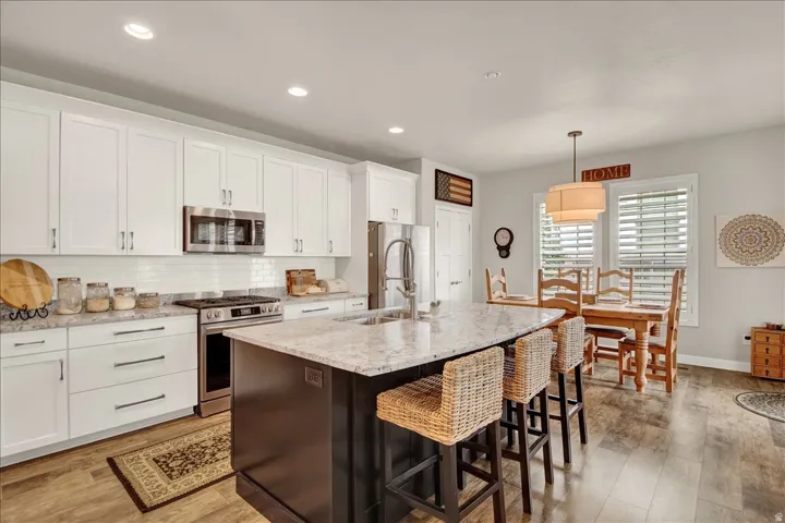 Kitchen featuring white shaker-style cabinetry, granite countertops, stainless steel appliances, and wood-finish flooring