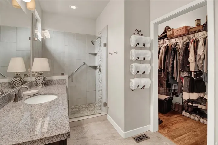 Bathroom featuring a granite-finish countertop with an undermount sink, a tiled walk-in shower with a glass enclosure, and a frosted glass window