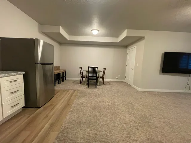 Recessed lighting, stainless steel refrigerator, white cabinetry with polished hardware, wood-finish flooring, and light-toned carpet