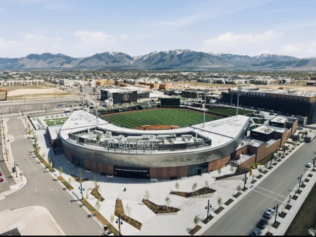Modern ballpark structure with a large green field, surrounded by urban development and distant mountains