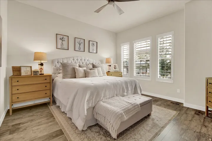 Spacious bedroom featuring wood-finish flooring, a ceiling fan, and three windows with plantation shutters