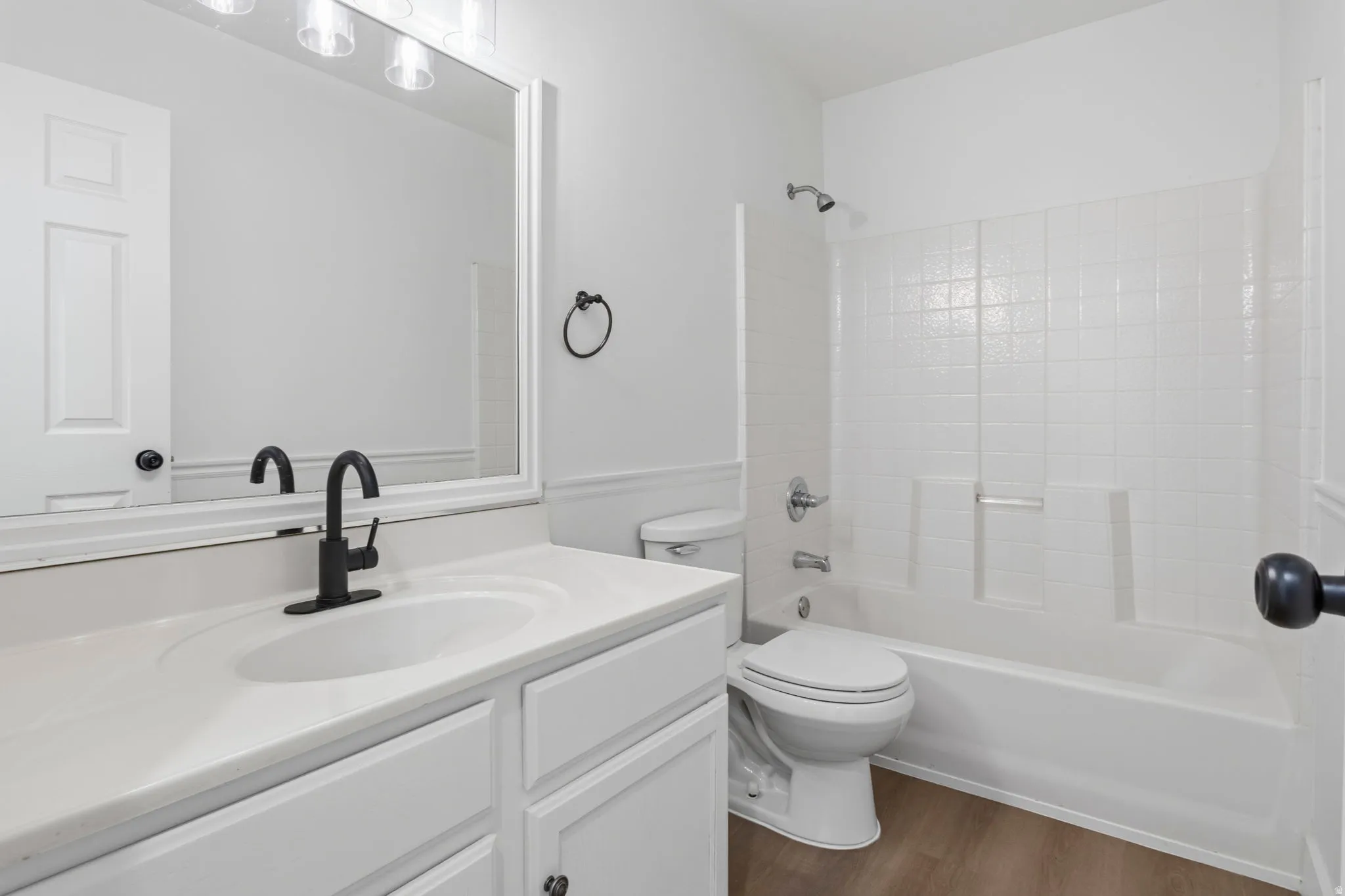 Bathroom featuring a white vanity with an integrated sink, matte black faucet, and a large mirror with overhead lighting