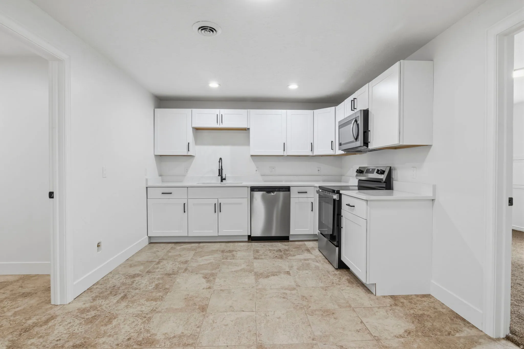 Contemporary kitchen featuring white cabinetry, stainless steel appliances, white subway tile backsplash, white countertops, and textured tile flooring