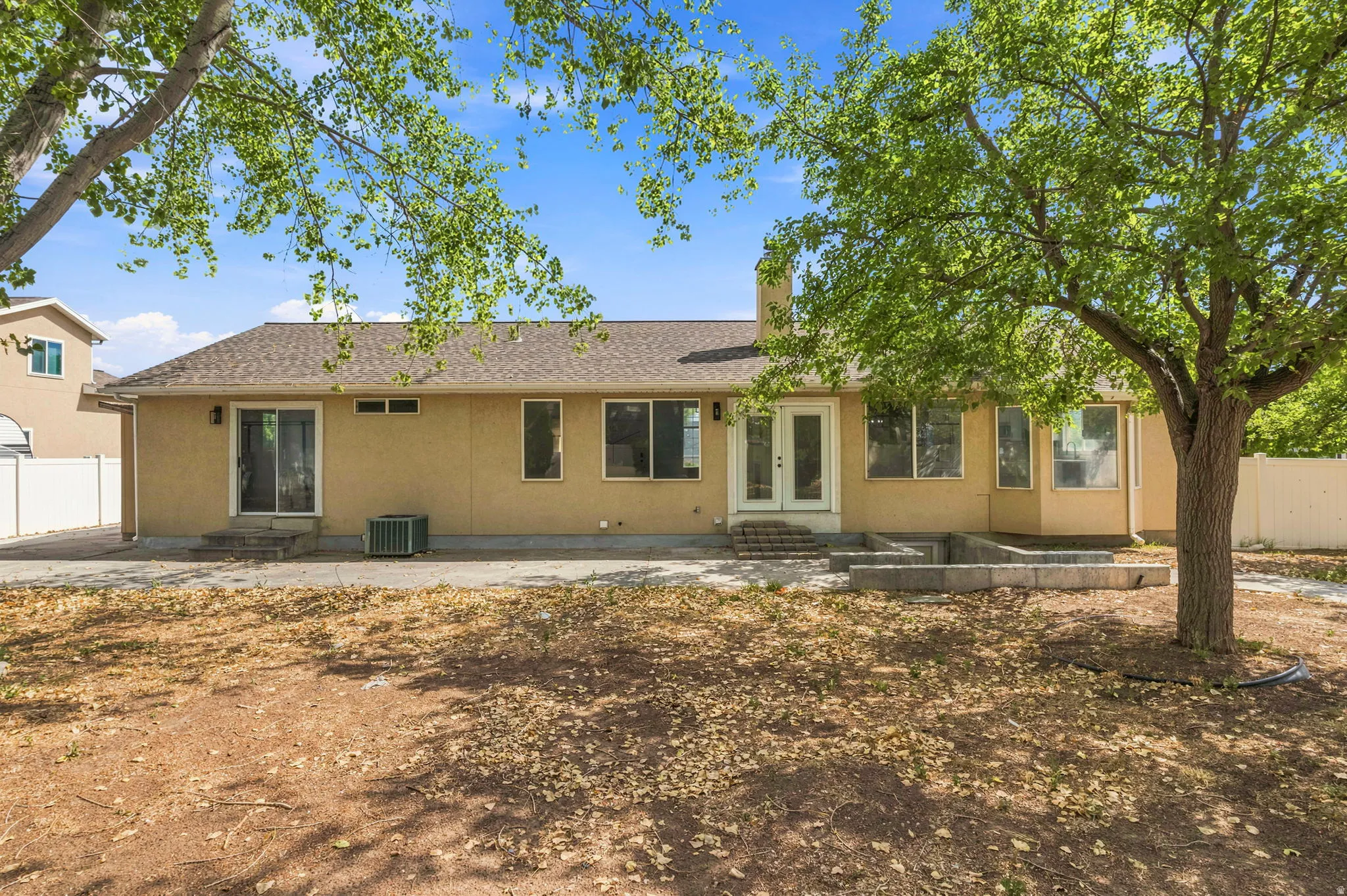 Rear exterior featuring a tan stucco finish, multiple windows, a sliding glass door, and a double entry door