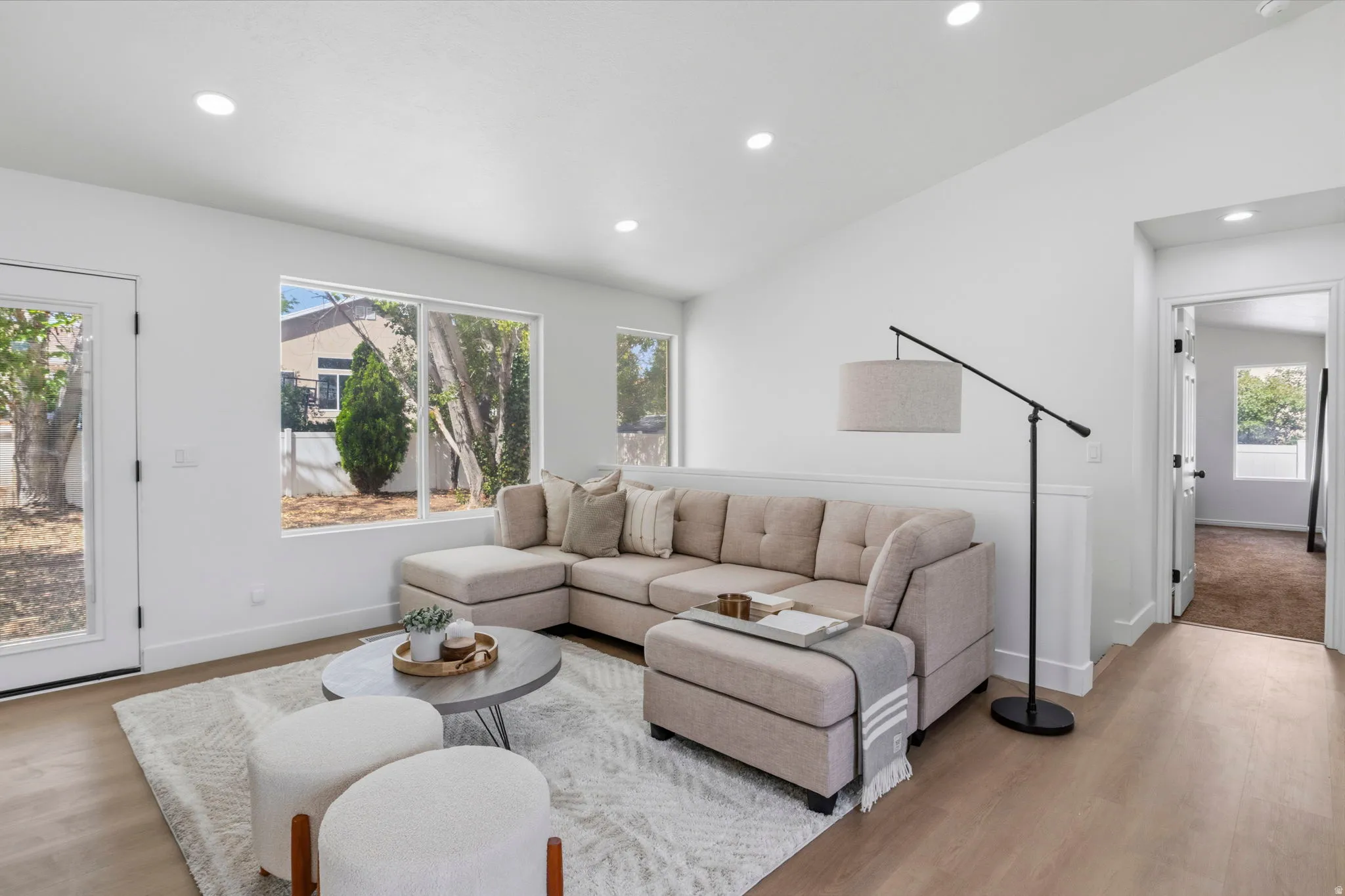 Bright living space featuring a vaulted ceiling with recessed lighting, wood-finish flooring, and a glass-paneled exterior door