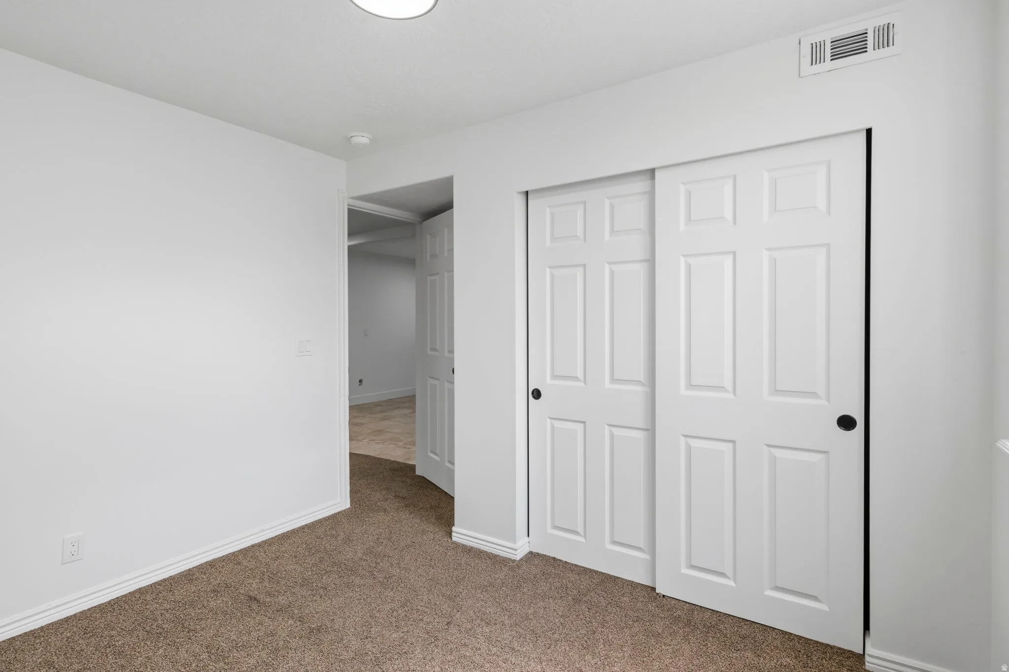 Neutral wall paint, plush carpet flooring, white baseboards, sliding panel closet doors, and recessed ceiling light fixture
