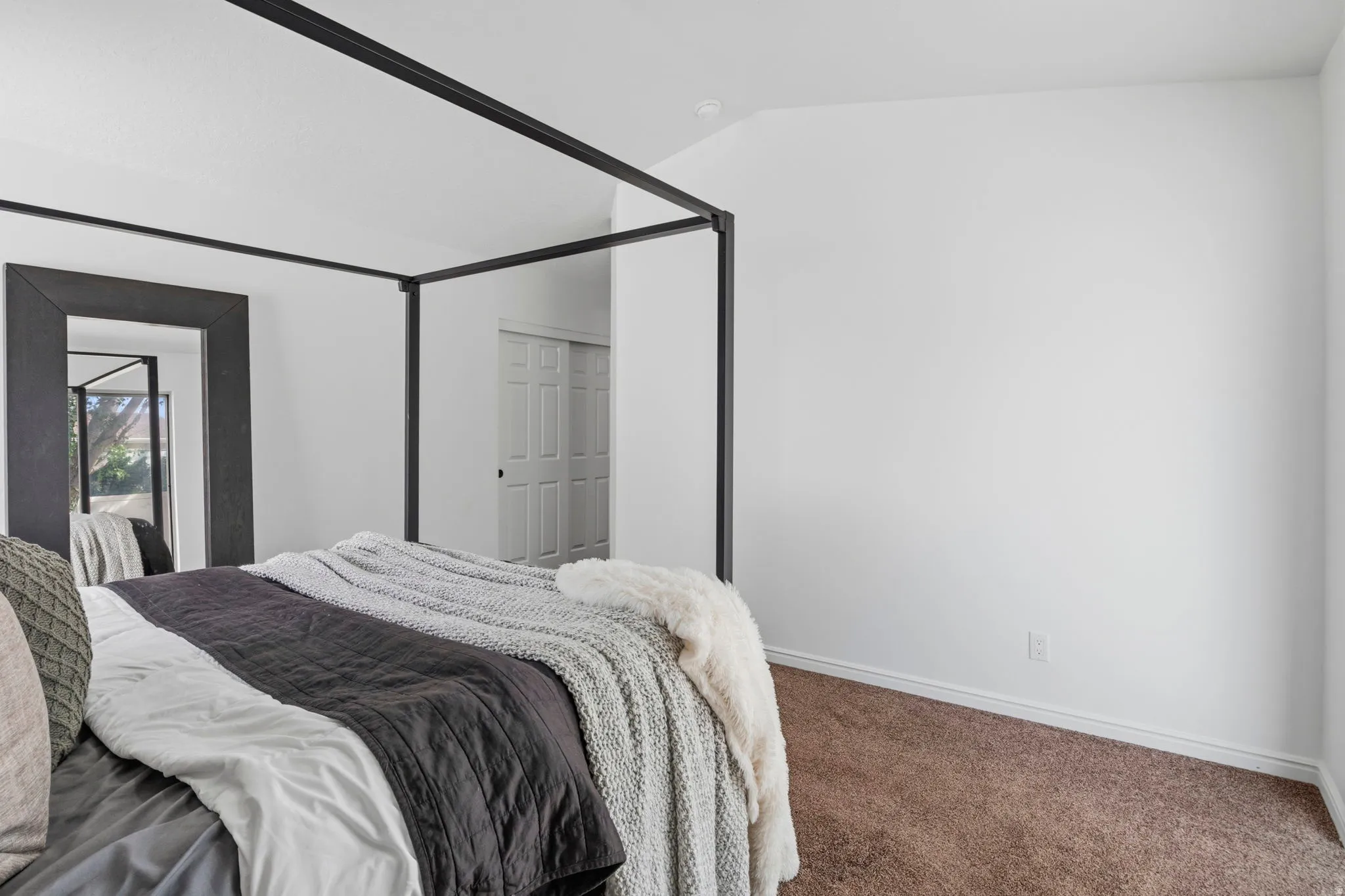 Spacious room featuring vaulted ceilings, neutral white walls, and brown carpet flooring