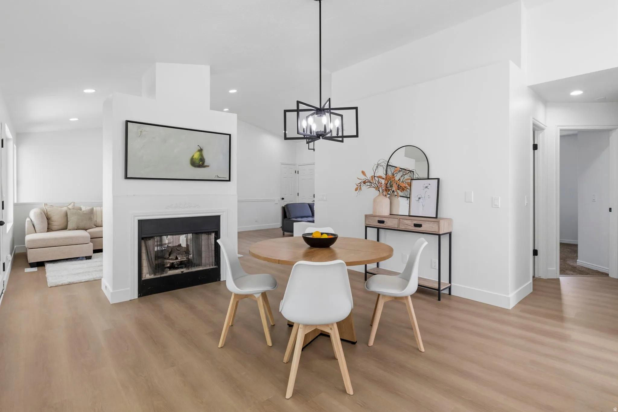 Open-concept living space with a central fireplace, light wood-finish flooring, recessed lighting, and a modern geometric chandelier
