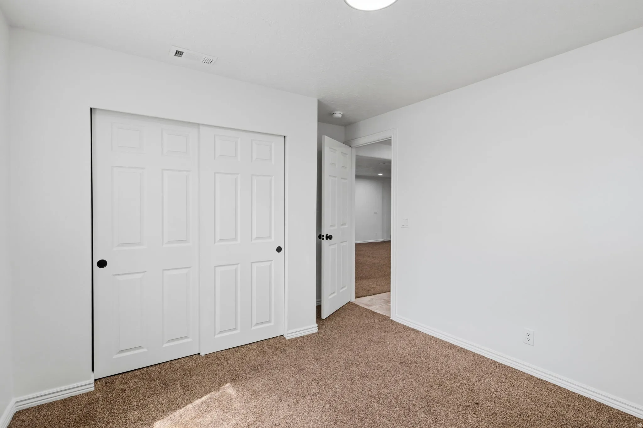 Bedroom featuring plush carpet flooring, white painted walls, a flush-mount ceiling light, and a two-panel sliding closet door with black hardware