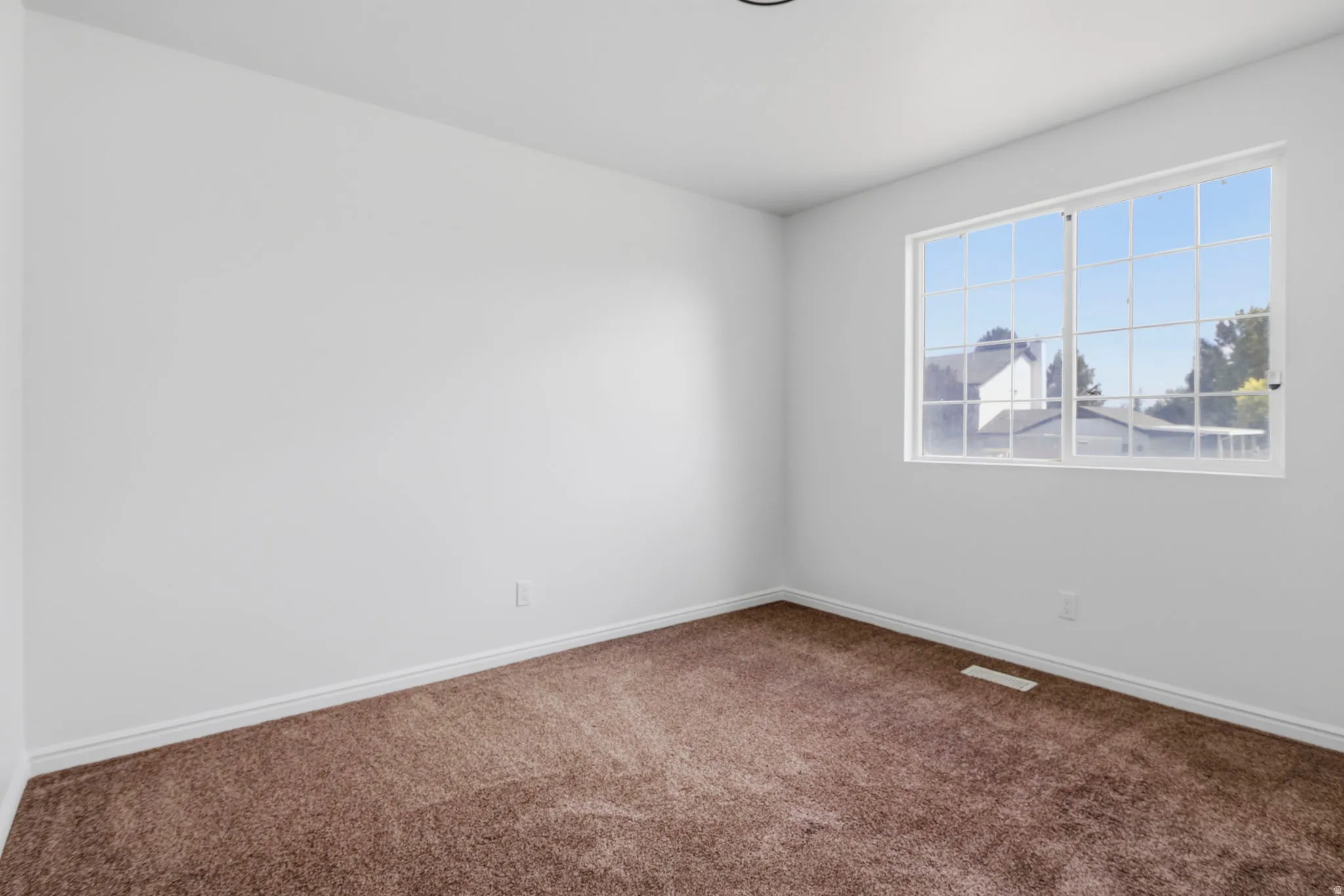 Spacious room featuring neutral paint, brown carpeting, white baseboards, and a large window with white muntins