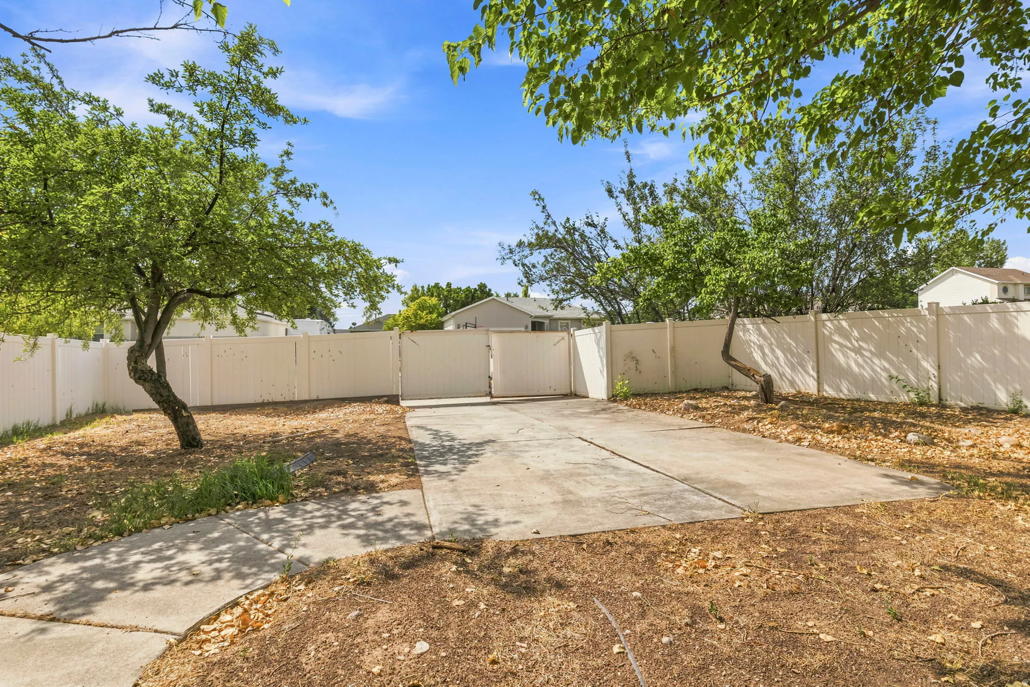 Paved concrete driveway with a double-gated entry, framed by mature trees and a perimeter fence